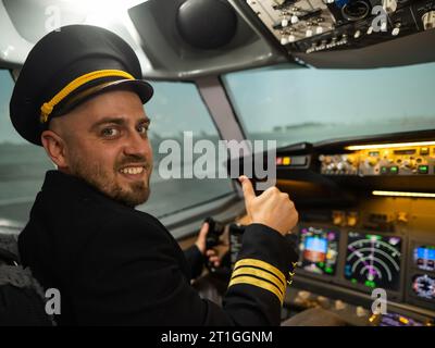 Kaukasischer bärtiger Mann, der beim Fahren eines Flugsimulators lächelt. Der Pilot im Cockpit zeigt Daumen nach oben. Stockfoto