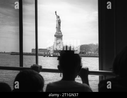 Ein junges Mädchen sieht die Freiheitsstatue durch ein Fährfenster in New York City, USA. Stockfoto