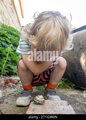 Ein kleiner Junge entdeckte eine Schnecke mit einer Muschel im Garten Stockfoto