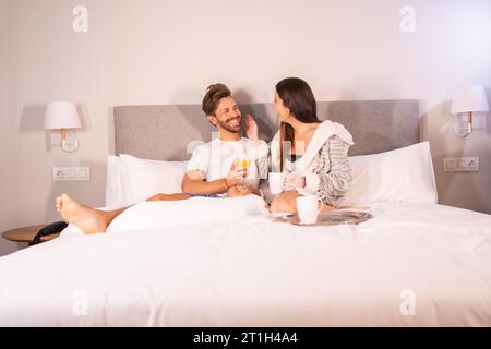 Ein liebevolles Paar im Pyjama, das morgens Kaffee und Orangensaft zum Frühstück im Hotelbett serviert, Lebensstil eines verliebten Paares Stockfoto