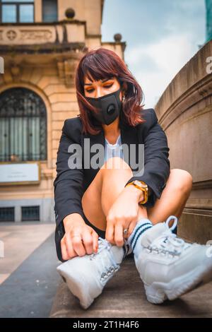 StreetStyle, eine junge Brünette mit Gesichtsmaske aus der Coronavirus-Pandemie. Dekonfination nach covid-19 Stockfoto