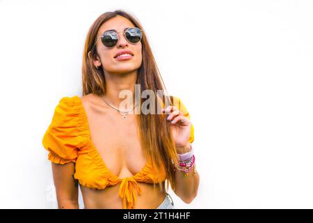 Lebensstil einer jungen kaukasischen Brünette mit orangem T-Shirt, Sonnenbrille und kurzer Hose auf weißem Hintergrund, mit Kopierraum und Sticks Stockfoto