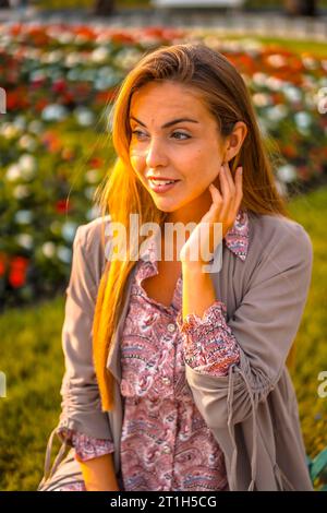 Lifestyle, ein junger Unternehmer. Kaukasisch und blond mit kastanienbraunem Regenmantel und Blumenkleid in der Stadt. Luftaufnahme neben Blumen in einem wunderschönen Stockfoto