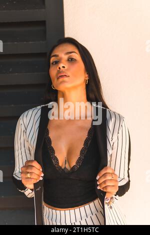 Lifestyle, glatthaariges lateinamerikanisches Brünette-Mädchen in weißem Anzug und schwarzen Streifen. Halb weißer und halb schwarzer Hintergrund. Miranda senxual, anders Stockfoto
