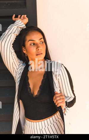 Lifestyle, glatthaariges lateinamerikanisches Brünette-Mädchen in weißem Anzug und schwarzen Streifen. Halb weißer und halb schwarzer Hintergrund. Miranda senxual, anders Stockfoto