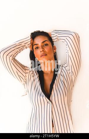 Lifestyle, glatthaariges lateinamerikanisches Brünette-Mädchen in weißem Anzug und schwarzen Streifen. Auf weißem Hintergrund. Auf die Kamera schauen, in anderen Stockfoto