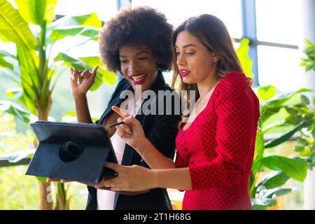 Junge unternehmungslustige Mädchen, kaukasische blonde und schwarzhäutige Mädchen mit Afro-Haaren, die mit einem Tablet einen Videoanruf machen. Lifestyle, Arbeit mit Good Stockfoto