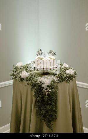 Eine Hochzeitstorte mit weißen Rosen, die auf einer grünen Tischdecke sitzt Stockfoto