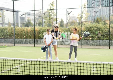 Aktive junge Frau, die Padel Tennis mit einer Gruppe von Spielern auf dem Tennisplatz im Freien übt Stockfoto