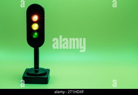 Miniatur-Ampel mit rotem, orangefarbenem und grünem Licht. Studio-Aufnahme. Grüner, leerer Hintergrund. Stockfoto