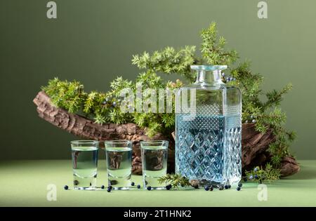 Blauer Gin in Karaffe auf einem Hintergrund von alten Schlingen und wacholderzweigen mit Beeren. Grüner Hintergrund mit Kopierraum. Stockfoto