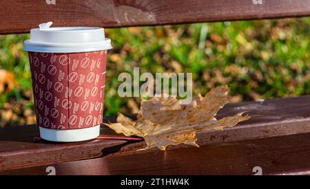 Papierbecher mit Kunststoffdeckel für Kaffee und Ahornblätter in Nahaufnahme Stockfoto