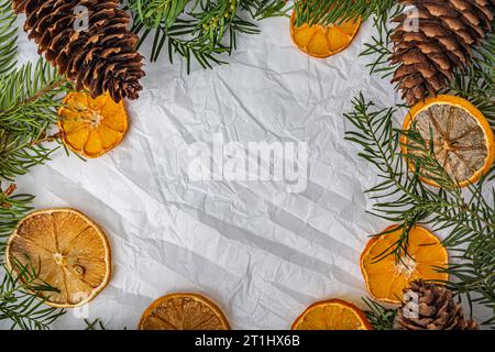 Fichtenzweige, Kegel und Orangen auf weißem zerknittertem Papier Stockfoto