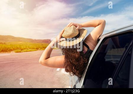 Rückansicht einer Frau, die sich aus ihrem Autofenster beugt, mit ausgestreckten Armen und Kopierraum Stockfoto