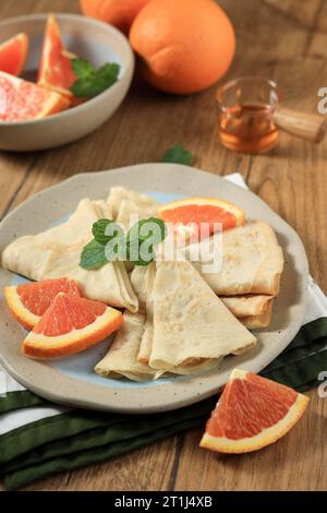 Crepes Suzette, dünne Pfannkuchen mit Orangensauce auf braunem Holztisch Stockfoto