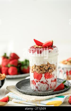 Erdbeerjoghurt Parfait mit Müsli, Minze und frischen Beeren im Glas auf weißem Holztisch. Gesundes Frühstückskonzept. Stockfoto