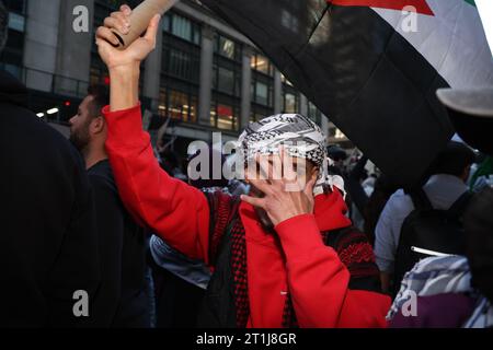 Ein palästinensischer Unterstützer bedeckt sein Gesicht, während er eine Flagge von Palästina schwingt, während Tausende von Menschen sich am Times Square versammeln, um gegen den anhaltenden Krieg zwischen Israel und der Hamas in New York City am 13. Oktober 2023 zu protestieren. (Foto: Gordon Donovan) Stockfoto