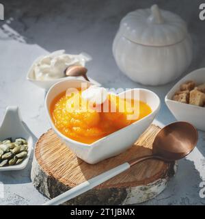 Kürbispüree Suppe mit Joghurt, Sesam und Kürbiskernen in einer herzförmigen Schüssel. Vegane Diät-Suppe für die ganze Saison. Stockfoto
