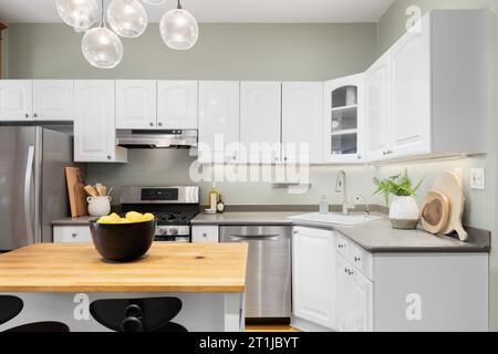 Ein Küchendetail mit weißen Schränken, Holzmetzgerblockinsel, grünen Wänden und einer darüber hängenden Leuchte. Keine Marken oder Etiketten. Stockfoto