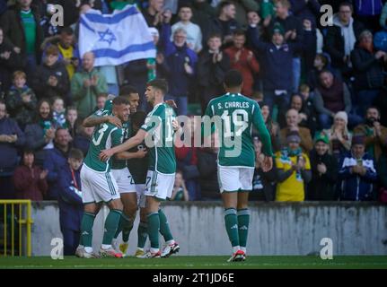 Der nordirische Josh Magennis (zweiter links) feiert mit seinen Teamkollegen, nachdem er seinem Team das zweite Tor des Spiels erzielt hat, während die Fans während des Qualifikationsspiels zur UEFA Euro 2024 im Windsor Park in Belfast eine israelische Flagge in den Tribünen schwenken. Bilddatum: Samstag, 14. Oktober 2023. Stockfoto