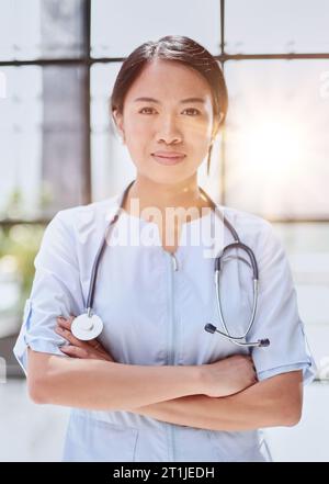 Porträt einer asiatischen Ärztin, die mit gekreuzten Armen auf die Kamera schaut Stockfoto