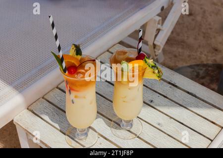 Zwei Gläser Cocktail auf weißem Tisch am Sandstrand unter Sonnenliege. Curacao. Stockfoto