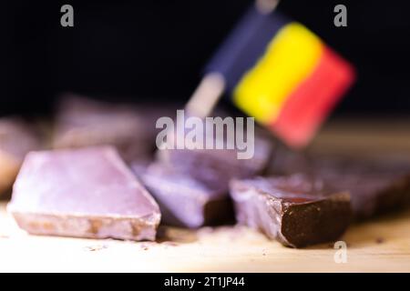 Ein helles Porträt einiger grober geschnittener Stücke leckerer brauner, dunkler belgischer Schokolade, die auf einer hölzernen Oberfläche liegen, mit etwas verschwommenem belgischem Fl Stockfoto