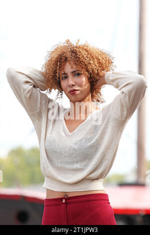 Außenporträts einer blonden Frau mit lockigem Haar mit weißem Pullover und roter Hose Stockfoto