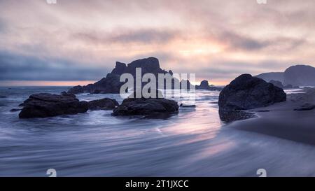 Sonnenuntergang am South Beach im Harris Beach State Park in Brookings, Oregon, mit Pastelltönen am Himmel, Felsbrocken und Meeresstapeln. Stockfoto