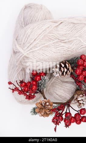 Graue Wollknäuel oder Garn aus Wolle mit Zweig roter Beeren und Tannenzapfen auf weißem Hintergrund. Handgefertigt, stricken, Hobby. Kopierbereich Stockfoto