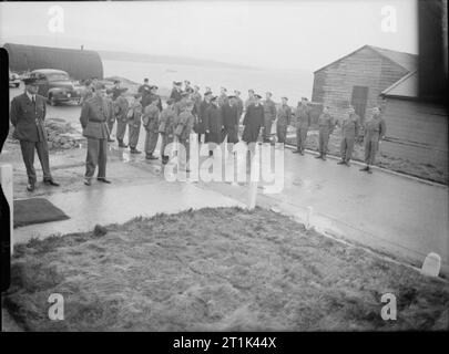 Die Royal Navy während des Zweiten Weltkriegs HM König George VI auf seinem Weg der Naval Kantine am Ufer bei Scapa Flow zu prüfen. Soldaten sind die Aufmerksamkeit auf beiden Seiten der Weg stand er nach unten geht. Scapa Flow selbst kann im Hintergrund gesehen werden. Stockfoto