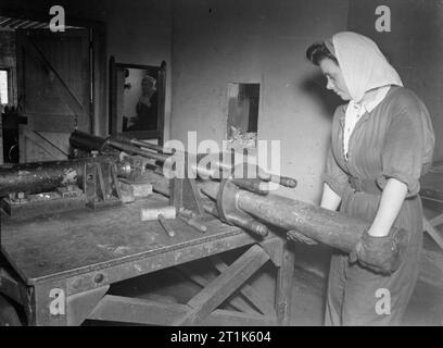 Leben an der Königlichen Marine Rüstung Depot Priddy ist hart, Gosport, 25-30 Juli 1944 Am RNAD Priddy ist hart, Gosport, einige Jobs sind so gefährlich, dass sie nur mit Hilfe der Fernbedienung durchgeführt werden. Hier ein Mädchen ist eine shell und Patrone in eine Maschine, die Sie auseinander ziehen. Die Maschine wird durch eine 18-Zoll dicke Mauer und wird über die Fernbedienung funktionierte umgeben. Im Spiegel der Mann, arbeitet er mit seinem Hebel stehen. Stockfoto