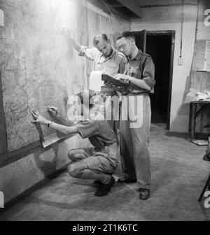 Stabsoffiziere plotten Truppe Positionen während der Invasion Siziliens auf einer Landkarte in der unterirdischen Technikraum auf Malta, 9. Juli 1943. Operation Husky: Die Sizilien Landungen 9 - 10 Juli 1943: Szene in der u-bahn Arbeiten in Malta, die koordinierte Operation Husky. Drei britischen Offizieren Grundstück Positionen auf großen Schautafeln. Die Zimmer war in einer der Höhlen auf Malta als ein Luftangriff vorsorglich entfernt. Stockfoto
