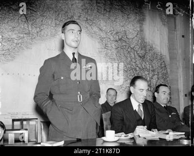 Royal Air Force Bomber Command, 1942-1945. Wing Commander J B 'Willy' Tait, Kommandierender Offizier der Nr. 617 Squadron RAF, gibt seinem Konto des erfolgreichen Raid auf das deutsche Schlachtschiff TIRPITZ in Tromsø, Norwegen Fjord (Katechismus) am 12. November 1944, während einer Pressekonferenz im Ministerium für Information, London. Saß neben Tait, in Zivil, ist Air Commodore H A Jones, Direktor für Öffentlichkeitsarbeit an der Luft Ministerium. Das Sitzen auf Jones' links ist Squadron Leader ein G Williams, der Nr. 9 Squadron RAF-Led auf dem Raid. Stockfoto