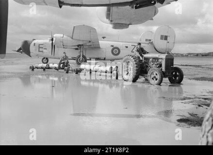 Royal Air Force Coastal Command-Nr. 247 Gruppe Operationen in der Azoren, 1943-1945. Ein RAF Traktor abschleppen trolleyloads Tiefe - Abgaben, verhandelt über eine überschwemmte disperal Bereich zwischen den konsolidierten Befreier GR Mark gegenüber von Nr. 220 Squadron RAF geparkt bei Lagens. KG 904" ZZ-E' steht im Hintergrund. Stockfoto