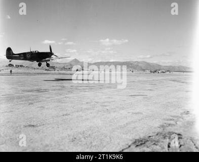 Royal Air Force in Malta, Gibraltar und das Mittelmeer, 1940-1945. Supermarine Spitfire Mark VC, EF 566 'G', von Nr. 335 (Griechische) Squadron RAF landet in Heraklion, Kreta, zu tanken und - Arm während der sammelmittelübertragung Operationen gegen die deutsche Besatzung im Nordwesten der Insel Re. Vickers Wellington kann man vor und auf der rechten Seite geparkt werden. Stockfoto