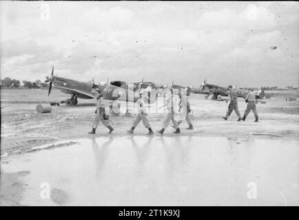 Royal Air Force in den Fernen Osten, 1941-1945 Piloten von Nr. 607 Squadron RAF, der Rückkehr von einem Sortie gegen japanische Truppen versuchen, die Sittang-fluß zu überqueren, (die Schlacht von Sittang-fluß Bend), vorbei an der Supermarine Spitfire Mark VIIIs im Monsun - überflutet Flugplatz bei Mingaladon, Burma. Stockfoto