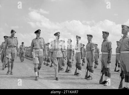 Royal Air Force Operationen im Nahen Osten und in Afrika, 1939-1943. King George VI prüft einer Ehrenwache der RAF Regiment bei der Ankunft in Hammamet, Tunesien, bei seinem Besuch in Nordafrika. Die große Gestalt auf der linken Seite ist die Air Commodore L F Sinclair, Kommandierender Offizier der taktischen Bomber Kraft von der Nord-westlichen Alliierten Tactical Air Force. Zu seiner Rechten, in der Ferne, Sir Arthur Tedder, der Commander-in-chief, mediterrane Air Command, Spaziergänge hinunter die Linie der Flieger. Stockfoto