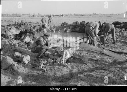 Royal Air Force - 2nd Tactical Air Force, 1943-1945. Ein RAF Officer untersucht von fahrzeugtruemmern aus der ersten Deutschen Kampfjets, die von der RAF erschossen zu werden, wie Royal Engineers bereiten Wasser aus dem Krater, der durch seine Auswirkungen in einem Feld süd-westlich von Nijemegen, Holland Links zu entleeren, in der Suche nach weiteren bleibt. Das Flugzeug, eine Messerschmitt Me 262 von Hauptmann Hans-Christoff Buttman 1 geflogen./KG (J) 51 eine patrouille von fünf Supermarine Spitfire Mark IXs von Nr. 401 Squadron RCAF gefallen war, unter der Leitung von Squadron Leader R I A Smith, am Vortag. Stockfoto