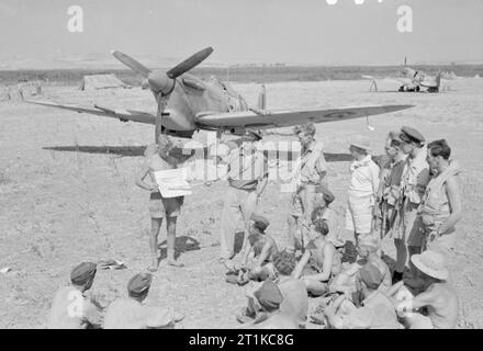 Royal Air Force - Italien, auf dem Balkan und in Südosteuropa, 1942-1945. Flying Officer C L Collings, Offizier in der Wüste Air Force Malaria Control Unit, Vorträge für Piloten und Bodenpersonal der Nr. 152 Squadron RAF auf Verteidigung Taktik gegen die Krankheit, vor einer der Squadron Supermarine Spitfire Mark VCs in Mascali, Sizilien. Stockfoto