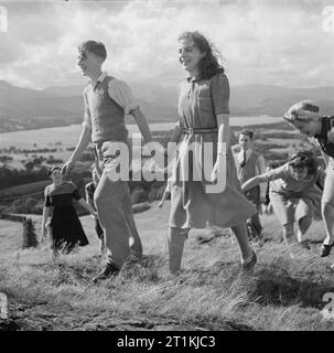 Co-operative Jugend Sommer Schulen - zu Fuß um Windermere, England, 1943 ein Teenager Paar halten Hände, als Sie zu Fuß durch die Landschaft rund um den Lake Windermere mit einer Gruppe von Freunden nach dem Unterricht am Morgen an der Summer School sind vorbei. Sie alle scheinen viel Spaß zu haben, obwohl es ein wenig Wind gefegt, und genießen die Aussicht auf den See und die Hügel dahinter. Stockfoto