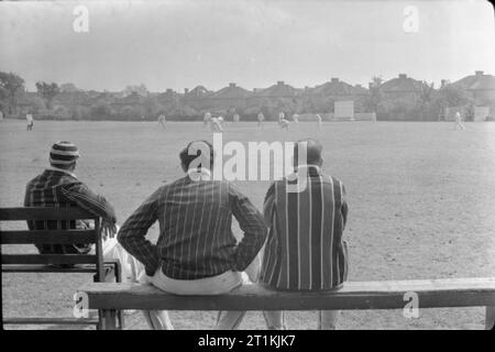 Cricket Match-Abdeckung von einer Übereinstimmung zwischen Kenton und Alexandra Park, Kenton, Middlesex, England, UK, 1945 Drei Zuschauer auf den Bänken vor dem Pavillon (nicht sichtbar) in der Sonne sitzen ein Cricket-spiel zwischen Kenton und Alexandra Park an der Kenton Boden, Harrow, Middlesex zu beobachten. Das Spiel kann im Hintergrund zu sehen. Stockfoto