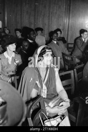 Reich - und Welt - Party - Radio Broadcast von der Overseas Club, St James's, London, 1942 Frau K C Roy hört die Nachricht aus der Halle von Indien bei der Overseas Club. Frau Roy ist aus Bengalen und hat einen Sohn, ist ein Offizier in der Armee. Hinter ihr, eine Gruppe von West afrikanische Techniker gesehen werden kann, genießen die Unterhaltung. Stockfoto