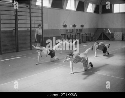 Werk wohl Arbeit - Wohlfahrt an die Pilkington Glass Factory, St Helens, Lancashire, England, Großbritannien, 1944 Frauen Stretching Übungen in der Sporthalle in der Fabrik Rehabilitation Centre, (vermutlich auf der Pilkington Glas arbeitet bei St Helens), als Teil ihrer Erholung nach einer Verletzung. Sie sind kniend auf dem Boden, mit einem Bein und dem anderen Arm ausgestreckt. Nach dem ursprünglichen Titel' das Ziel der [center] ist, um Männer und Frauen aus dauerhaft deaktiviert zu verhindern. Durch Übungen und Massagen unter der Leitung des physio-Therapeuten in modernen Methoden der verletzten Personen ar geschult Stockfoto