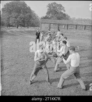 Erste US-Armee Rehabilitationszentrum - Erholung und Ausbildung bei 8 Erholungsheim, Stoneleigh Park, Kenilworth, Warwickshire, Großbritannien, 1943 B Grad Auszubildende am 8.Erholungsheim, Stoneleigh Park engagieren sich in einem Anfall von Boxen in den Sonnenschein, als Teil ihrer Freizeit körperliches Training und Rehabilitation. Sie stehen in einer Linie außerhalb der Kaserne, von ihrem Ausbilder und einen kleinen Hund bewacht. Wird der Besoldungsgruppe B Auszubildende, Sie sind jetzt fast wieder zu voller Eignung: Sobald Sie einen Grad erreichen, können sie zum Militärdienst zurück. Stockfoto