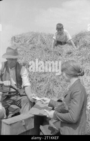 Ein Dorf speichert - die nationalen Ersparnisse in Lewknor, Oxfordshire, England, 1941 Frau Amor, ein Mitglied der lokalen Einsparungen Ausschuss, verkauft Briefmarken zu speichern Bauer Robert Graham, über den Hof. Herr Graham ist auf seinem Traktor und ein Junge, vielleicht der Bauernsohn, der an der Spitze eines großen Haufen Heu sitzt, beobachten die Transaktion. Stockfoto