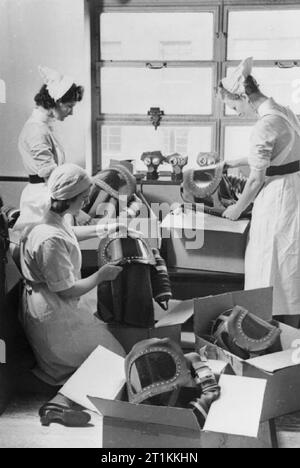 Gas Bohren in einem Londoner Krankenhaus - Gasmasken für Babys geprüft werden, 1940 Krankenschwestern an einem Londoner Krankenhaus baby gas Atemschutzmasken für einen Bohrer bereit zu entpacken. Auf der Fensterbank, ihre eigenen Gasmasken gesehen werden kann. Auf der rechten Seite jedes Maske, der Balg Anordnung, die das Kind mit Luftzufuhr würde gesehen werden kann. Dieses Rohr benötigt gepumpt werden, so dass das Kind atmen konnte. Stockfoto
