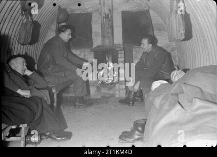 Home Guard Mann Anti Aircraft Gun - Zivilschutz in Großbritannien, 1943 eine Gruppe von Home Guard vor dem Feuer in ihren Nissen Hütte entspannen. Ein Mann schläft auf sein Feldbett, die anderen sitzen um zu chatten und sich vor dem Feuer warm, während ihre Stiefel zu entfernen. Stockfoto