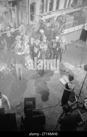 Afs-Film Schauspieler: die Verfilmung von "unveröffentlichte Story' in Denham Film Studios, Denham, Buckinghamshire, England, Großbritannien, 1941 Regie Harold Französisch (links) gibt letzte Anweisungen an die Schauspieler am Set von "Unveröffentlichte Story' in Denham Film Studios. Die Stars der beiden Städte Film Unternehmensfilm, Richard Greene und Valerie Hobson, können gerade gesehen, hören von Harold Französisch unter einer Gruppe von Hilfs Film Service Extras. Im Vordergrund rechts, den Durchgang Mädchen gesehen werden kann, die Verfolgung der Verfahren. Stockfoto