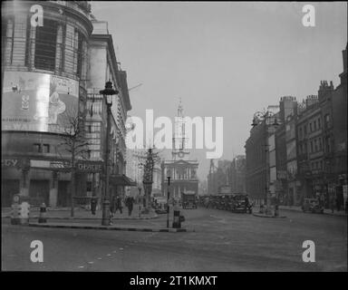 London wie üblich - den Alltag in London, England, 1940 einen weiten Blick über den Strand in London, östlich von Aldwych. Deutlich sichtbar sind die Gaiety Theatre auf der linken Seite und der Kirche von St Mary-le-Strang in der Mitte der Straße. Fußgänger vorbei das Theater und eine Reihe von Autos oder Taxis in der Mitte des Foto gesehen werden kann. Die kerbs auf der Verkehrsinsel in den Vordergrund wurden in Abschnitte in schwarz lackiert und weiß sie mehr Fußgänger sichtbar zu machen. Ein großer Krieg Einsparungen Poster an der Wand des Theaters gesehen werden. Stockfoto
